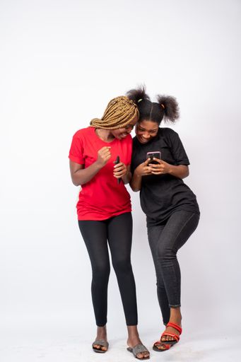 A pair of young African female friends looking at a phone and laughing isolated on a white background
