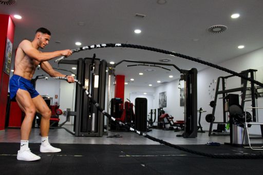 A young Caucasian boy training crossfit in a gym - hit exercise with ropes