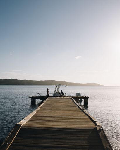A scenic view of a wooden pier extending into the sea with a boat docked and people enjoying the serene sunset.