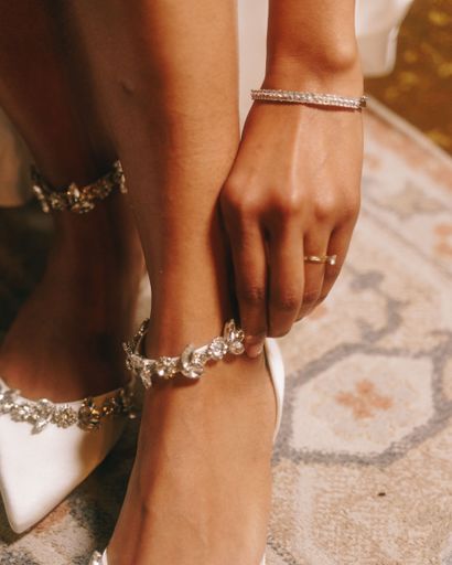 Close-up of a woman adjusting a sparkling anklet on her white high heels, showcasing elegant jewelry and fashion style.