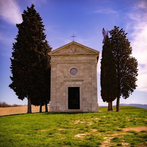 Chapel of Vitaleta in Tuscany surrounded by cypress trees under a clear blue sky, capturing serene beauty and architectural charm.