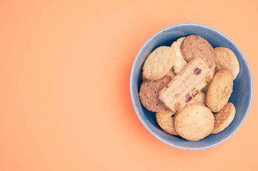 Vertical shot of organic biscuits in a blue bowl on orange surface with text space
