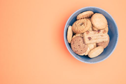 Vertical shot of organic biscuits in a blue bowl on orange surface with text space