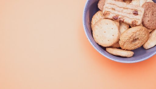 Vertical shot of organic biscuits in a blue bowl on orange surface with text space