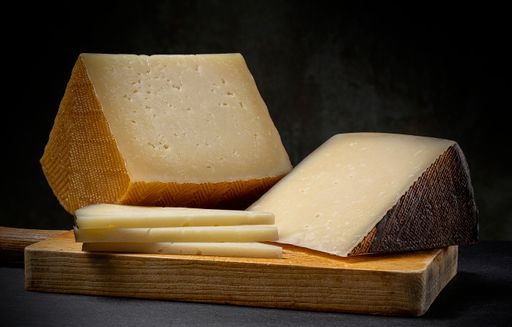 A closeup of two blocks of cheese on a wooden cutting board in front oa black background