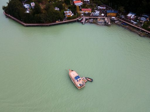 Aerial view of a boat on turquoise water near a coastal village with colorful houses and lush greenery in the background.