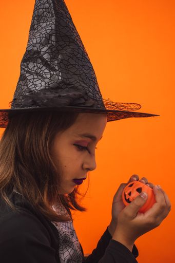A little witch holding a Halloween pumpkin on an orange background