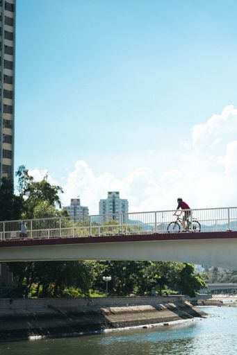 A vertical shot of a person riding a bicycle on the bridge over the river
