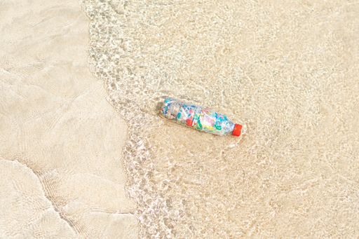 A top view of a bottle filled with microplastics on the shore of the beach
