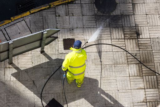 A high angle view of a Worker cleaning a street sidewalk with high pressure water jet machine