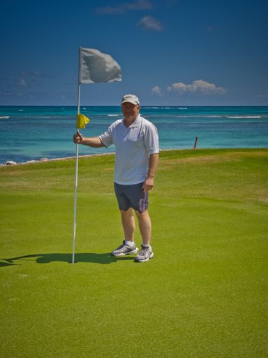 A vertical picture of a man standing on a golf course surrounded by the sea in the Dominican Republic