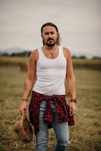 A young handsome Serbian male with a brown hat in his hand walking in a field