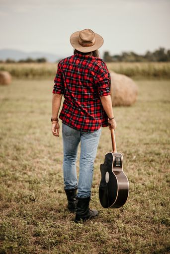 A young handsome Serbian male in a flannel shirt with guitar in his hand walking in a field