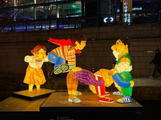Colorful lantern sculptures of children playing at night in Seoul, Korea, with illuminated buildings in the background.