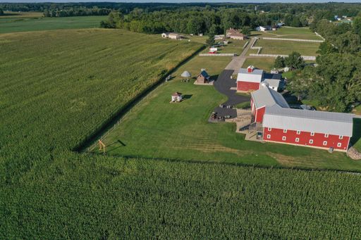 Aerial view of a rural farm with red barns surrounded by vast green fields under a clear sky.