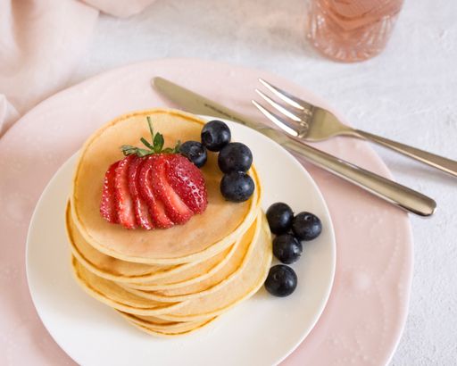Pancakes served on a plate with strawberry and blueberries.