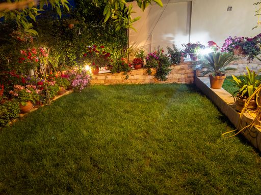Lush green lawn illuminated by hidden garden lights accentuating colorful flowers in plant pots.