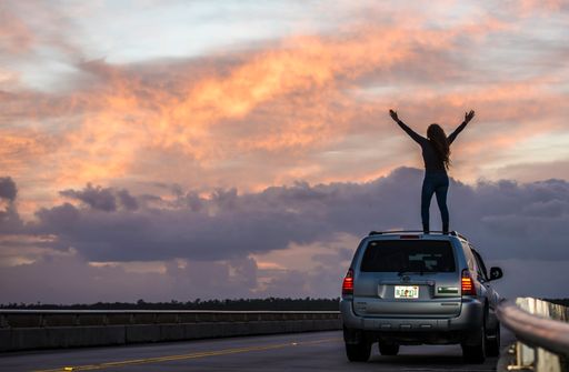 A silhouette of a young woman cheering the sunset on top of her car in the Everglades National park, Florida