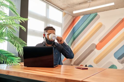 A young Latin man working from his living room using his laptop and having a coffee