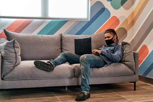 A young Latin man lying on the sofa and working with his laptop from the living room of his house