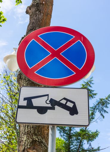 A low angle of a warning tow car and no parking sign with a tree trunk in the background