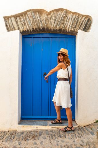 A young woman in a white dress sitting by a blue-painted door in Cadaques, Costa Brava