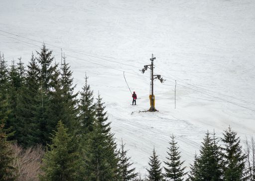 Snowy landscape with ski lift and lone skier in red on a slope