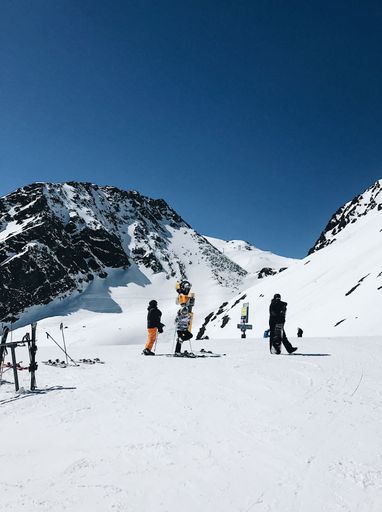 Skiers and snowboarders on a snowy mountain slope under a clear blue sky, enjoying winter sports in a scenic alpine setting.