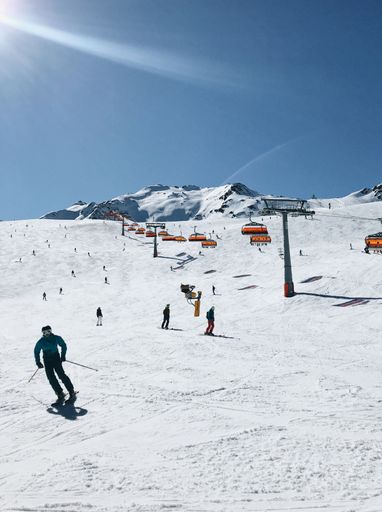 Skiers on a snowy slope with chairlifts under a clear blue sky in a mountain resort.