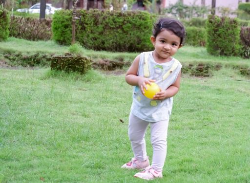 A little Southeast Asian girl playing with a yellow ball in a park