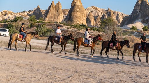 A group of people riding horses in Cappadocia with the scenery of fairy chimneys