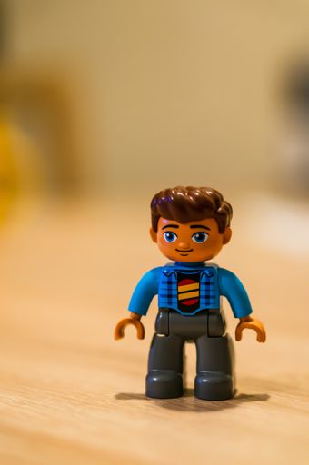 Plastic Lego Duplo man figurine standing on a wooden surface in soft focus background.