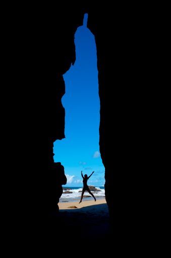 A vertical shot of a person jumping on the seashore seen through cliffs