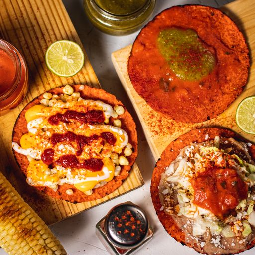 A vertical shot of three mini pizzas on wooden boards with lime, sauces, and powdered pepper