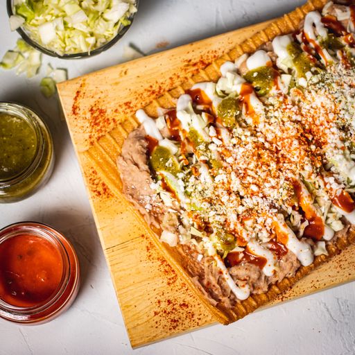 A vertical shot of a square pizza on a wooden board on a white table with sauces
