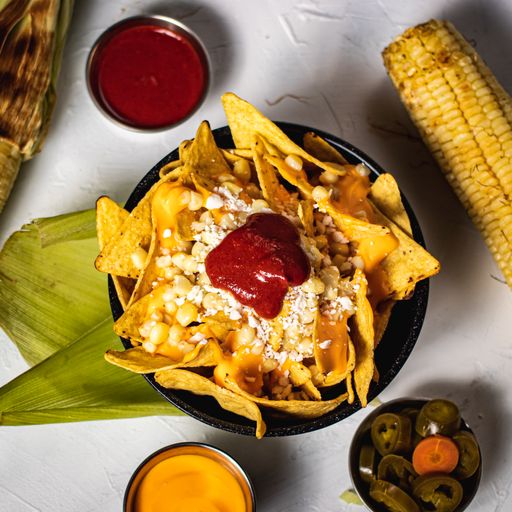 A vertical shot of delicious nachos with corn, sauces, pickled pepper and carrots
