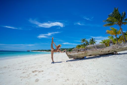 A young Caucasian female doing yoga at a white sand beach
