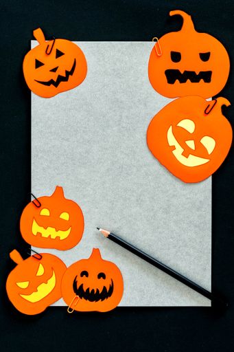 A closeup shot of a white paper with orange pumpkin decorations as a Halloween background
