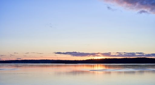 A serene sunset over a calm lake with a clear sky and distant silhouette of trees.
