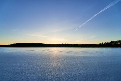 A serene winter landscape with a frozen lake under a clear blue sky at sunset.