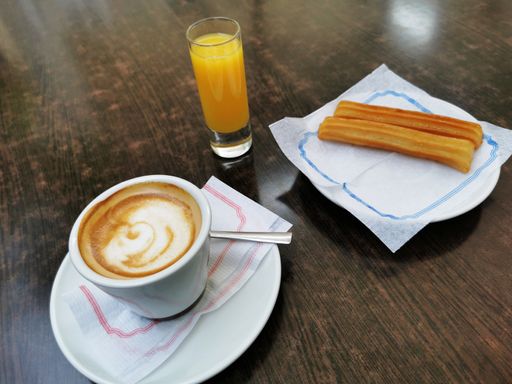 A cup of cappuccino, a glass of orange juice and churros on a wooden table