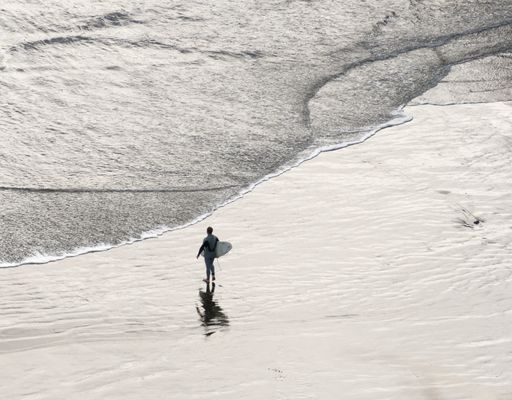 A surfer walking into the sea in New Zealand