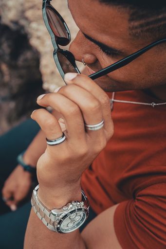 A beautiful shot of a young man taking off his sunglasses while sitting on the rocks near the lake