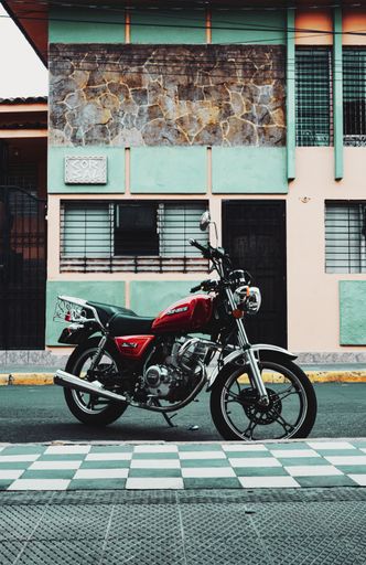 A vertical shot of a red motorcycle parked near a turquoise building in Alicante, Spain