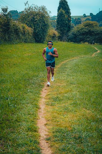 The young fit man with sunglasses winning and working out in the park while listening to music