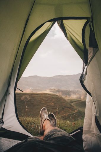 A beautiful vertical shot of a person's legs put out of a tent with a magical landscape view of fields