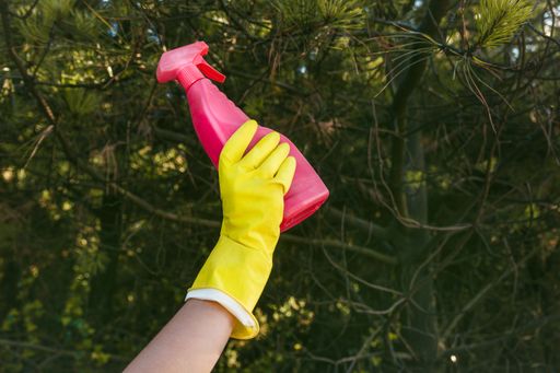 A female with yellow gloves holding a plastic cleaning spray bottle - plastic pollution concept
