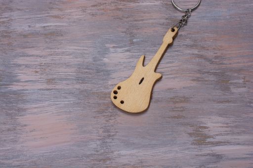 A closeup shot of a wooden guitar keychain on a surface with faded paint