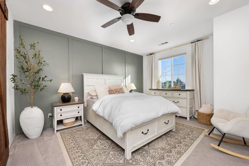 Modern bedroom interior with white furniture, green accent wall, and natural light through a window, creating a cozy and elegant atmosphere.
