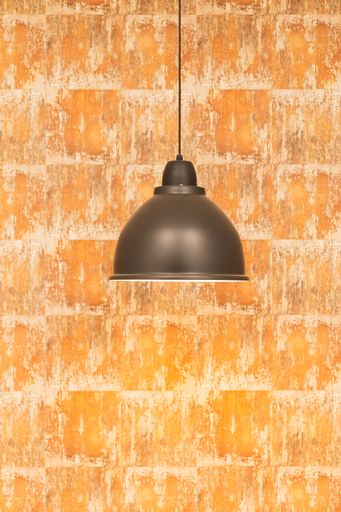 A vertical closeup of the black lamp hanging on the background of a textured orange wall.